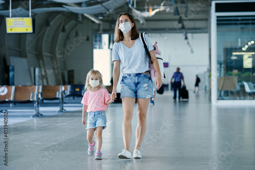 Mother with daughter in masks waiting for their flight at airport. Woman with little girl in international airport.