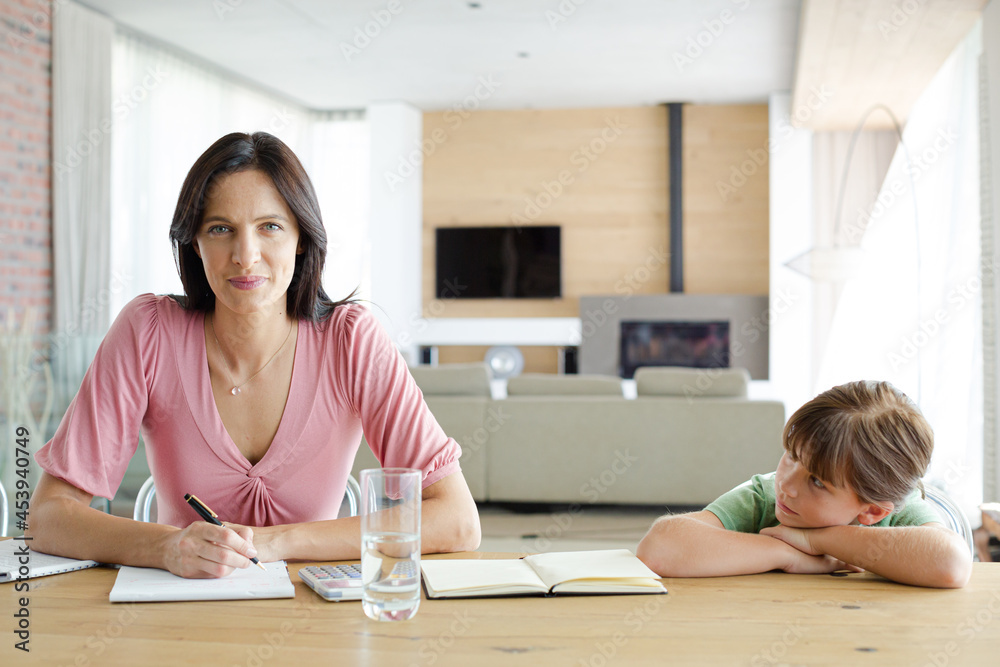 Woman sitting at table with daughter, using calculator Woman sitting at table with daughter, using calculator