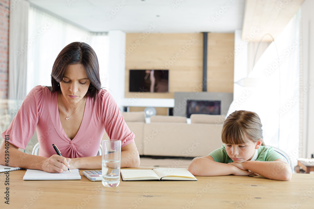 Mother sitting at table with daughter, using calculator Mother sitting at table with daughter, using calculator