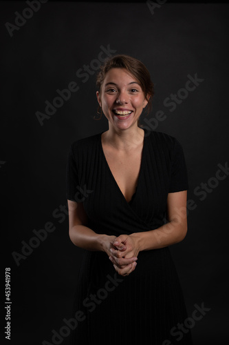 A young beautiful woman happy and smiling in a studio shot in black dress and background looking at the camera