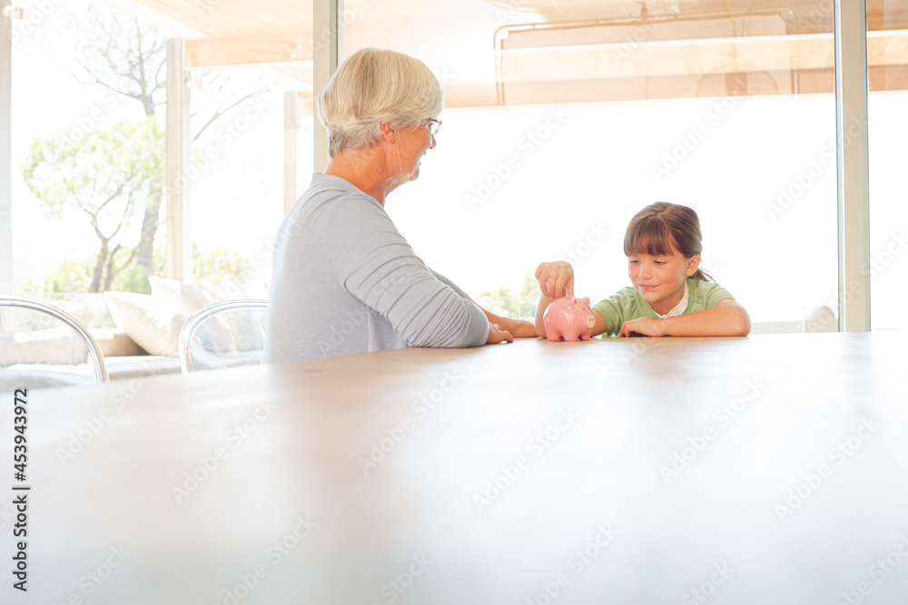 Obraz premium Older woman and granddaughter filling piggy bank