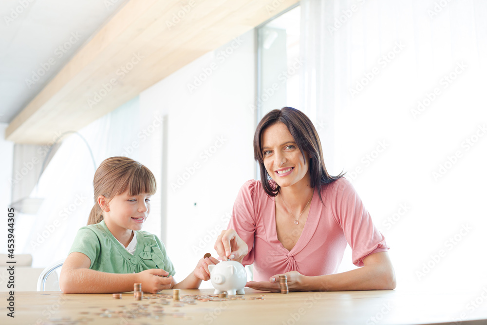 Mother and daughter filling piggy bank Mother and daughter filling piggy bank