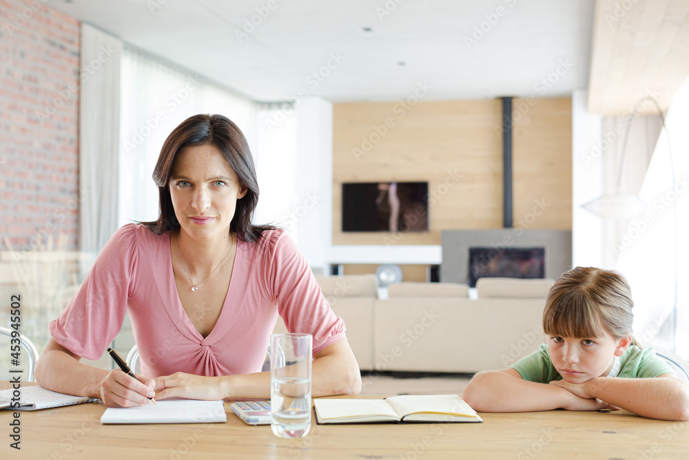 Mother sitting at table with daughter, using calculator Mother sitting at table with daughter, using calculator