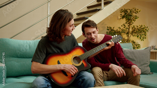 A young man is playing guitar for his friend and they both are singing
