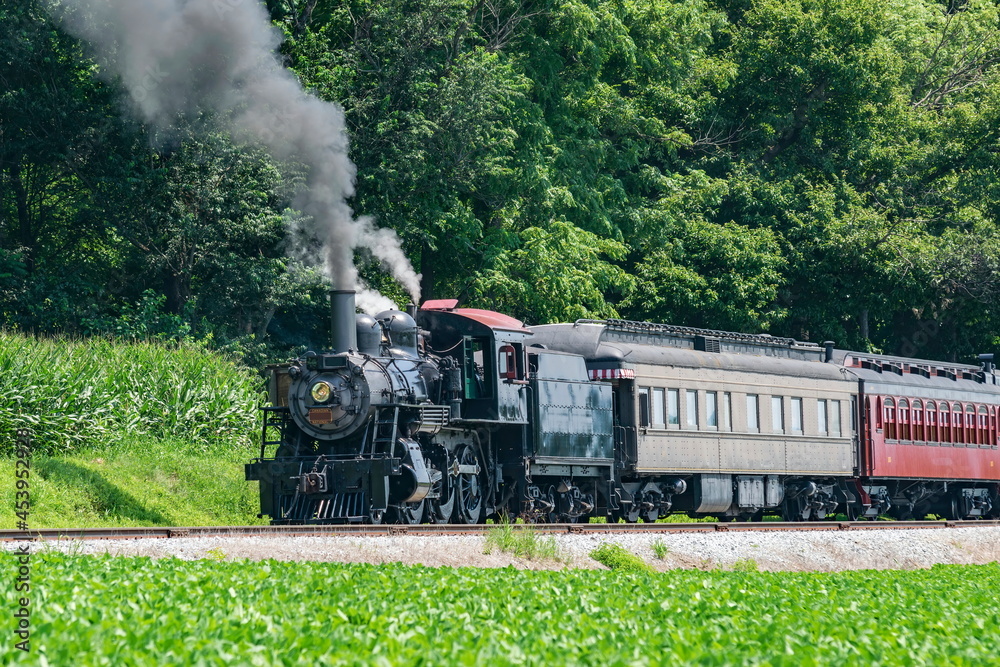 View of an Antique Restored Steam Passenger Train Blowing Smoke and Steam on a Sunny Summer Day