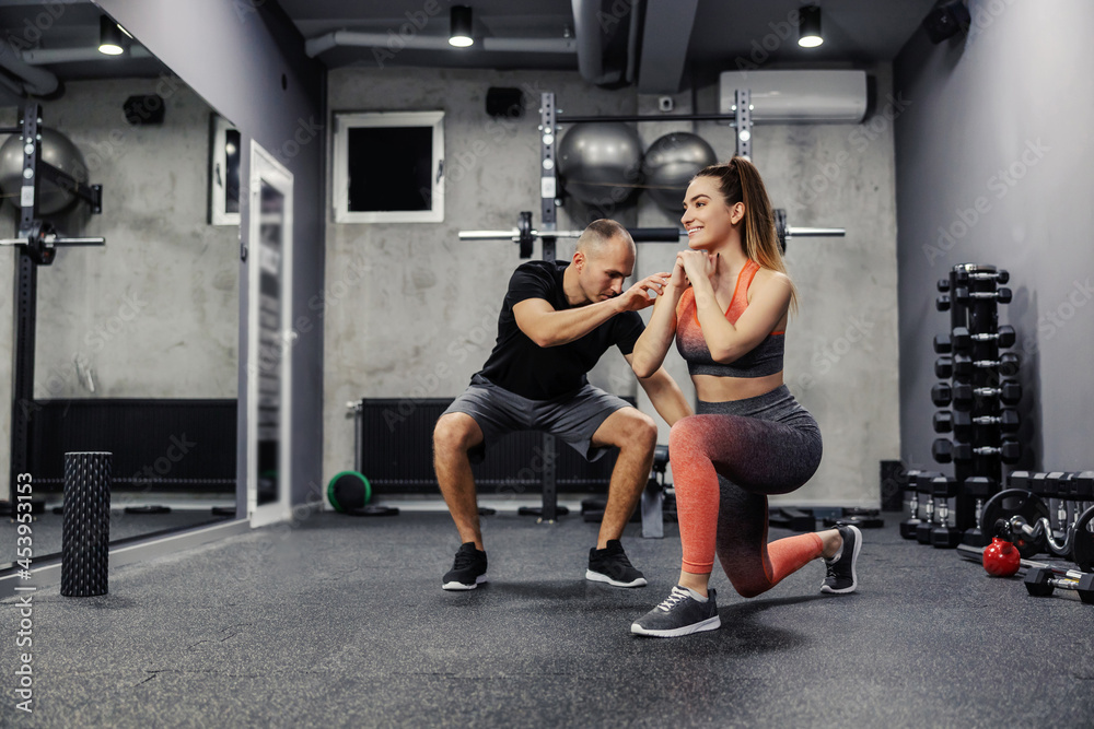 Obraz premium The concept of sports personal training. A fit man and a slender woman do sports exercises together. The lady stepped forward with her foot as the coach corrected her body position