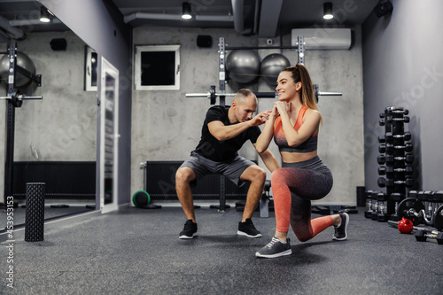 The concept of sports personal training. A fit man and a slender woman do sports exercises together. The lady stepped forward with her foot as the coach corrected her body position