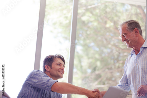 Older man and younger man smiling together at desk