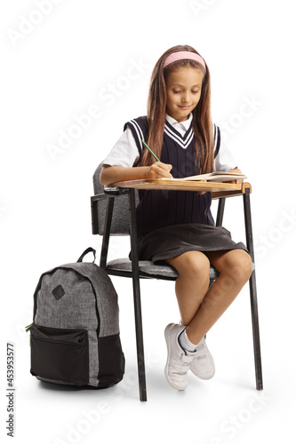 Beautiful schoolgirl sitting in a school chair and writing homework