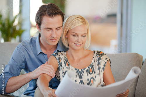 Couple examining blueprints together on sofa © KOTO