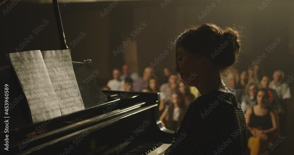 4K Footage Of Female Pianist Plays In Beautiful Grand Piano On Stage In Concert . A woman plays the piano in the concert hall . Many unrecognizable , blurred people in the background . 