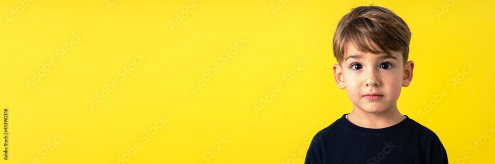 Front view portrait of small caucasian boy in front of yellow wall Front view portrait of small caucasian boy in front of yellow wall