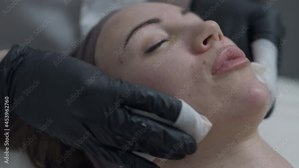 Close-up cleansing of beautiful female face in beauty parlor spa. Headshot portrait of relaxed satisfied Caucasian woman with closed eyes lying as male beautician taking care of facial skin Close-up cleansing of beautiful female face in beauty parlor spa. Headshot portrait of relaxed satisfied Caucasian woman with closed eyes lying as male beautician taking care of facial skin