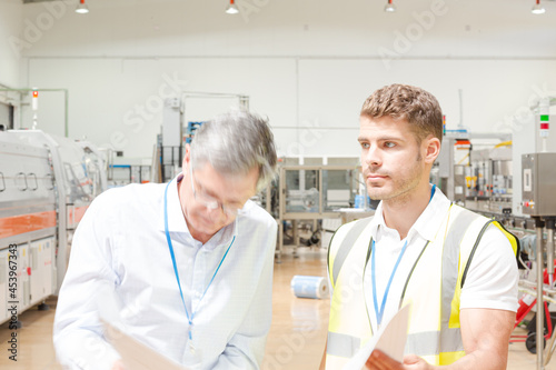 Supervisor and worker reading blueprints in factory