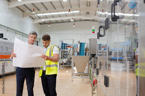 Supervisor and worker reading blueprints in factory