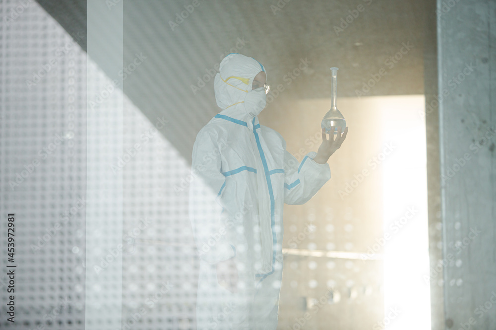 Fototapeta premium Scientist in clean suit examining liquid in test tube