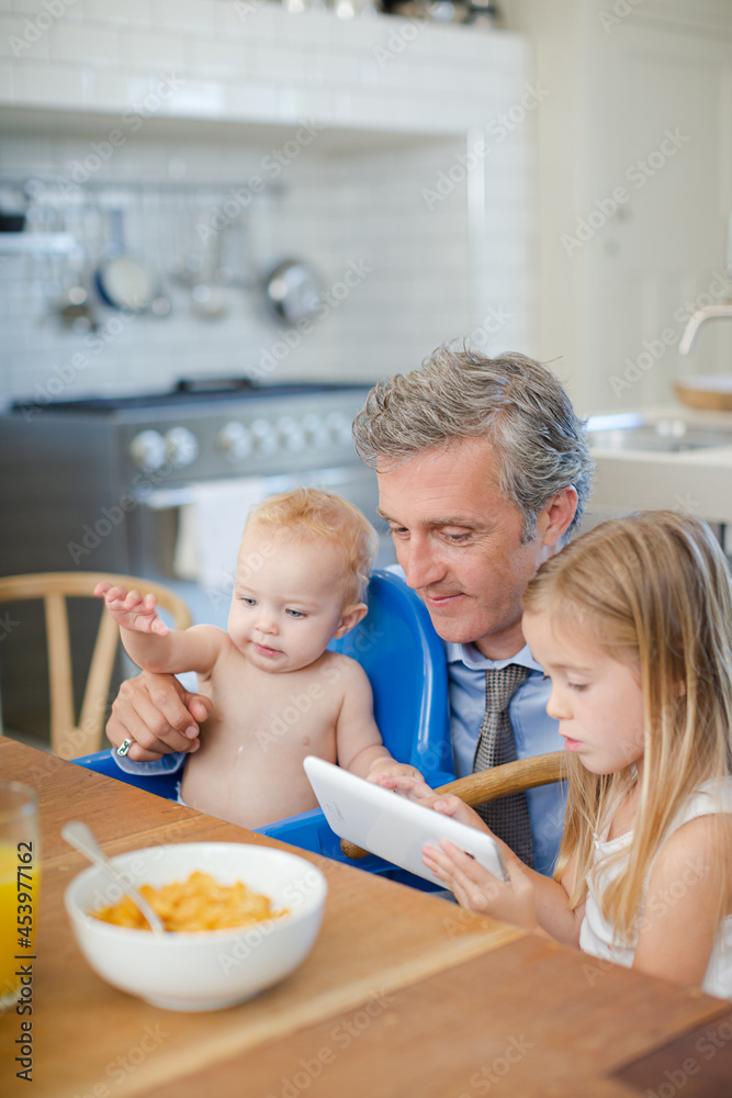 Father and children using digital tablet at table Father and children using digital tablet at table
