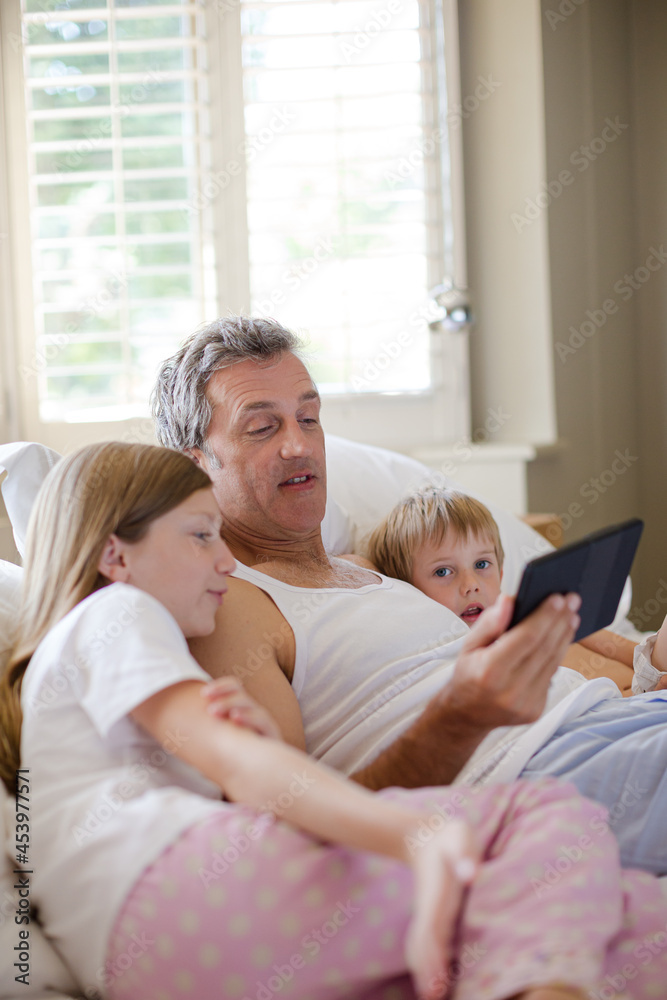 Father and children using digital tablet on bed Father and children using digital tablet on bed
