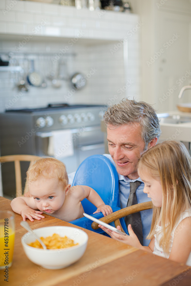 Father and children using digital tablet at table Father and children using digital tablet at table