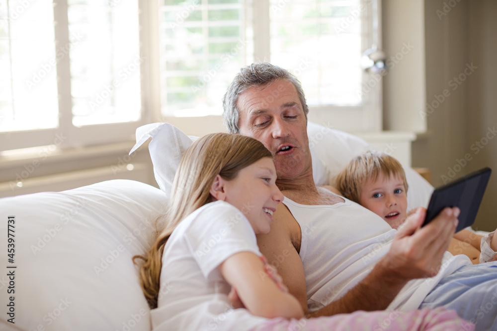 Father and children using digital tablet on bed Father and children using digital tablet on bed
