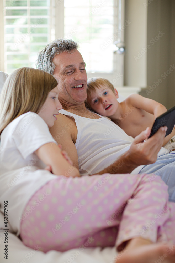 Father and children using digital tablet on bed Father and children using digital tablet on bed