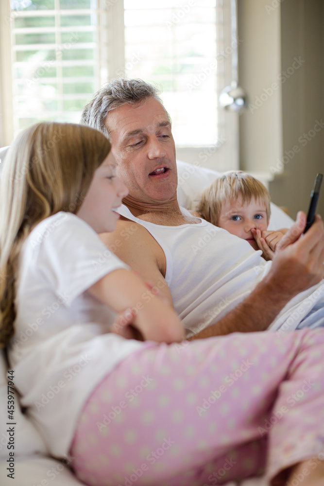 Father and children using digital tablet on bed Father and children using digital tablet on bed