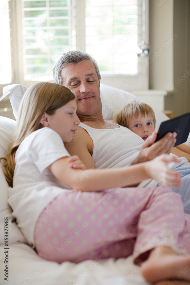 Father and children using digital tablet on bed