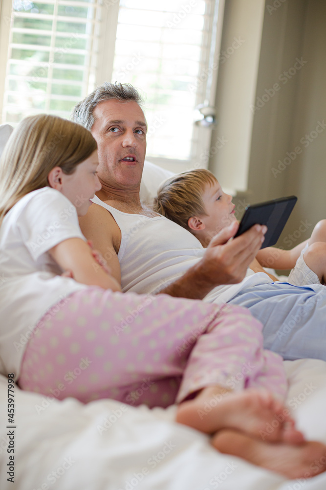 Father and children using digital tablet on bed Father and children using digital tablet on bed
