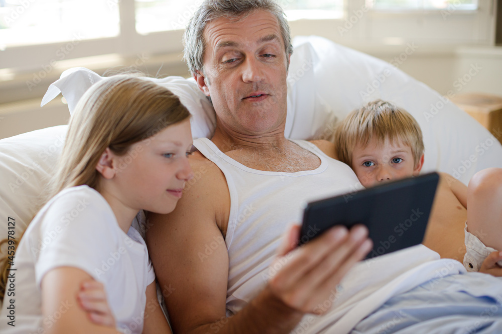 Father and children using digital tablet on bed Father and children using digital tablet on bed