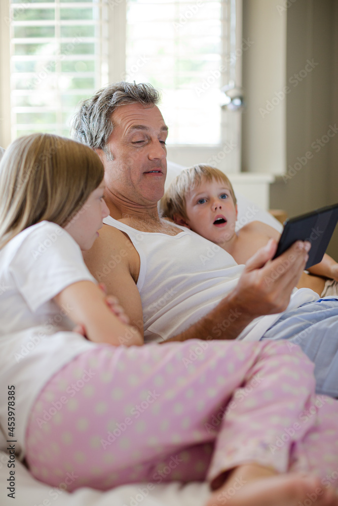 Father and children using digital tablet on bed Father and children using digital tablet on bed