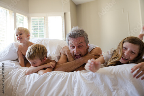 Father and children relaxing on bed © KOTO