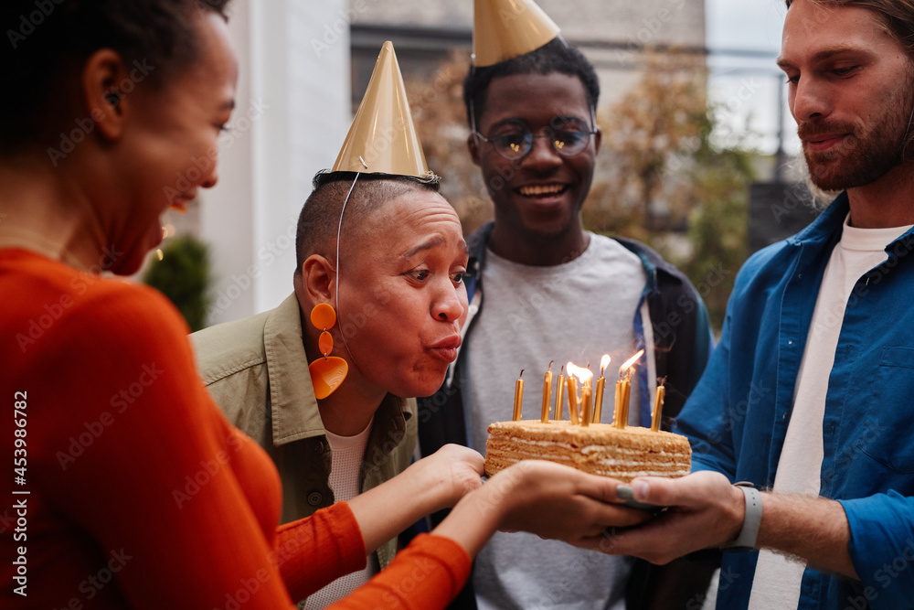 Diverse group of friends celebrating Birthday at rooftop party with woman blowing cake with candles