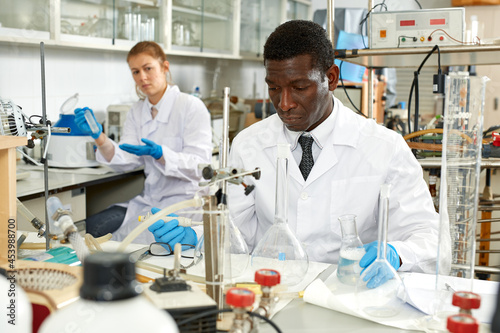 Proffesional male lab technicians with different glass tubes, girl on background