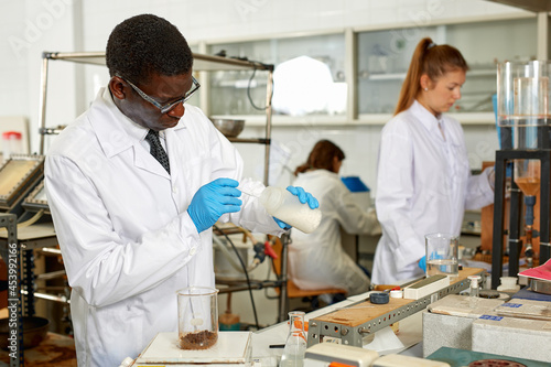 Focused male lab scientist in glasses working with different reagents  woman on background