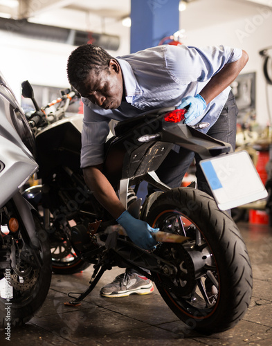 Afro american man working at restoring motorbike in motorcycle workshop. High quality photo
