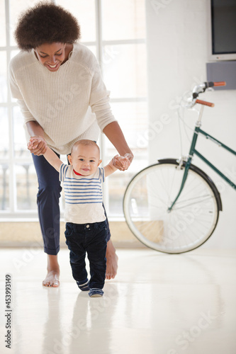 Mother helping baby boy walk in living room