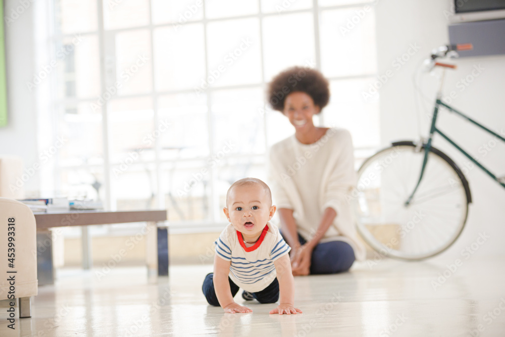 Fototapeta premium Mother watching baby boy crawl on floor
