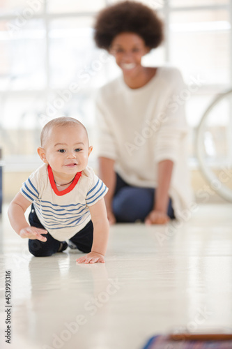 Mother watching baby boy crawl in living room