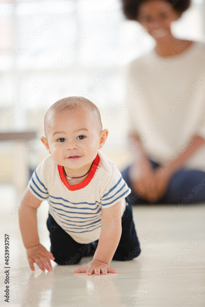 Mother watching baby boy crawl in living room Mother watching baby boy crawl in living room