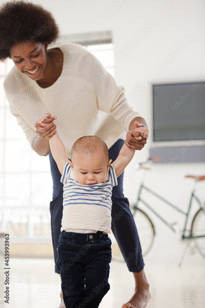 Fototapeta premium Mother helping baby boy walk in living room