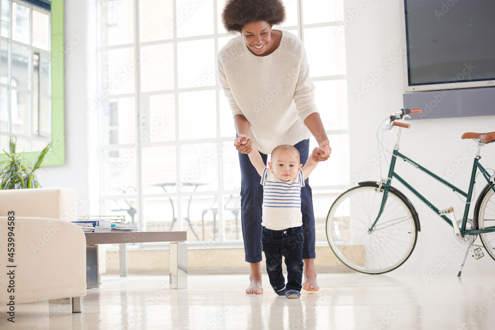 Mother helping baby boy walk on floor Mother helping baby boy walk on floor