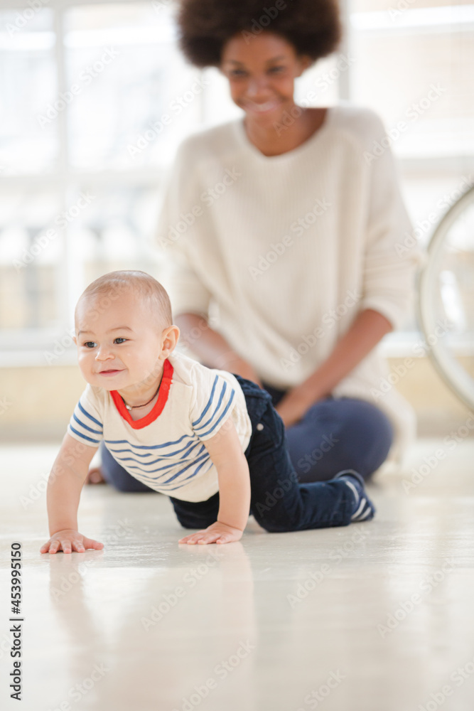 Mother watching baby boy crawl in living room Mother watching baby boy crawl in living room