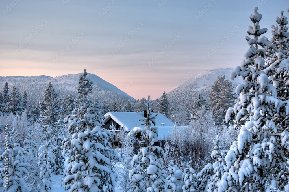 snow-covered landscape with trees, house and mountains in Lapland, Finland in winter