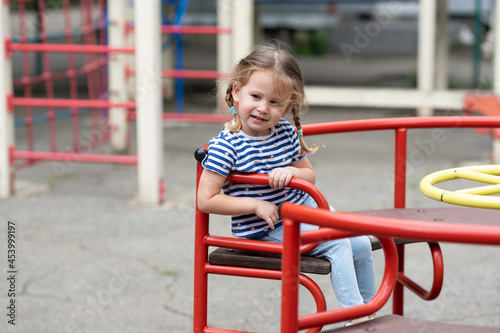 A cute little girl is whirling alone on a red  merry-go-round in a deserted playground. © Ольга Апанасенко