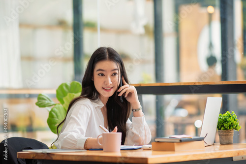 Young Asian female entrepreneur talking on the phone while working at home office.