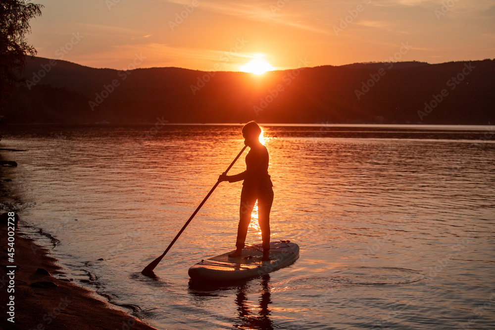 Girl on sup board with beautiful colored sunrise background mountains background