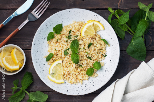 Boiled bulgur with fresh lemon and mint on a plate. A traditional oriental dish called Tabouleh. dark wooden background. top view