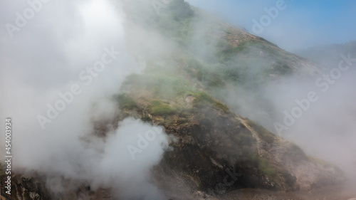 Valley of Geysers. Kamchatka. The mountain slopes are shrouded in thick steam from hot springs. Splashes of boiling water are visible. Blue sky in a fog. 