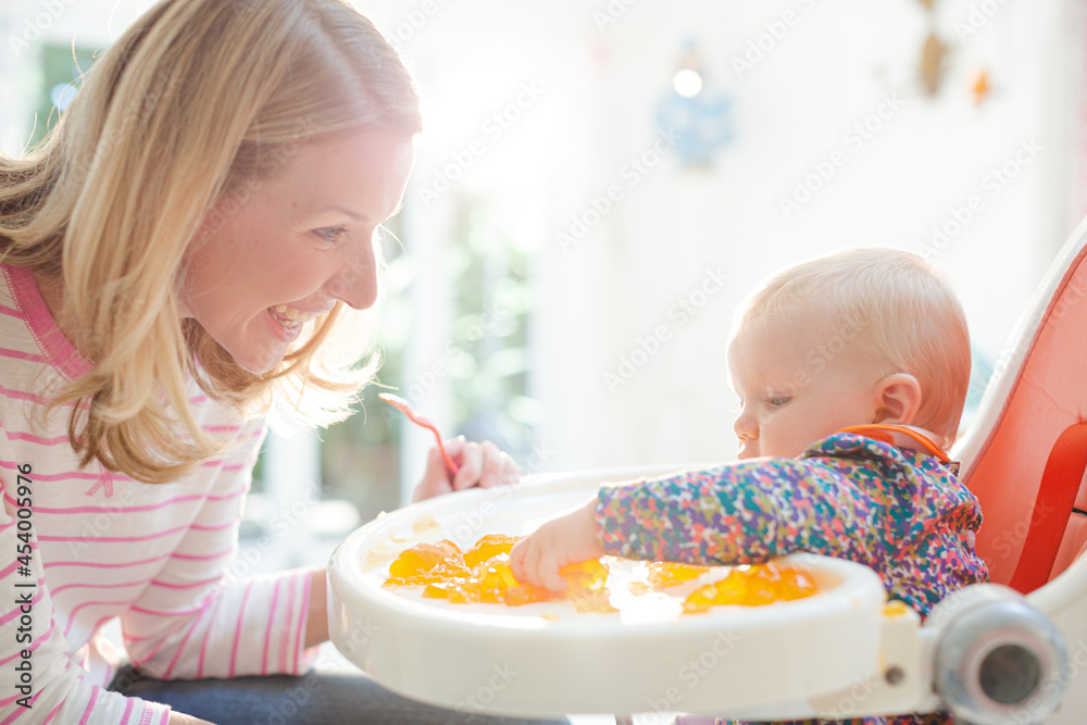 Mother feeding baby girl in high chair Mother feeding baby girl in high chair