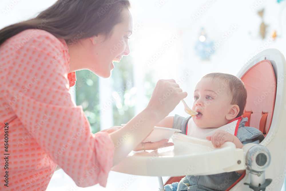 Mother feeding baby boy in high chair Mother feeding baby boy in high chair